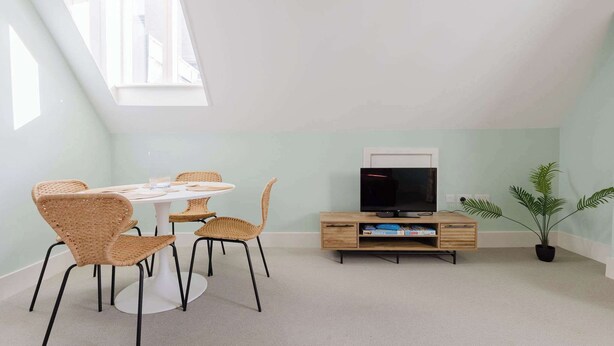 A room with a round table, four wicker chairs, a television on a wooden stand, and a potted plant. - Spacious 3BD Flat in Historic Building Shoreditch (Greater London)