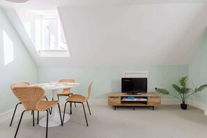 A room with a round table, four wicker chairs, a television on a wooden stand, and a potted plant.