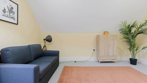 A room with a sofa, a lamp, a cabinet, a potted plant, and a framed picture on the wall. - Spacious 3BD Flat in Historic Building Shoreditch (Greater London)