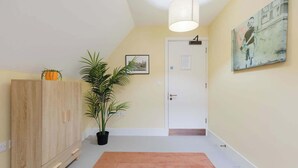 A hallway with a wooden cabinet, a potted plant, a framed picture, a door, and a painting on the wall.