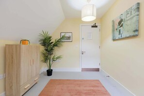 A hallway with a wooden cabinet, a potted plant, a framed picture, a door, and a painting on the wall. - Spacious 3BD Flat in Historic Building Shoreditch (Greater London)