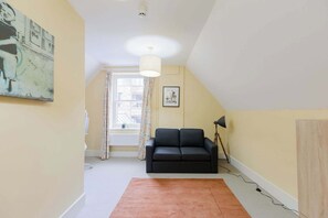 A room with a black sofa, a large window with curtains, a ceiling light, and a framed picture on the wall.