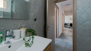 A modern bathroom with a white sink, a mirror, and a potted plant. - TelMar Sky View - “Stylish 3-Bedroom Apartment with Mountain & Sea Views” (Larnaka)