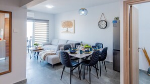 A modern living space with a dining area, a sofa, and a kitchen area. - TelMar Sky View - “Stylish 3-Bedroom Apartment with Mountain & Sea Views” (Larnaka)