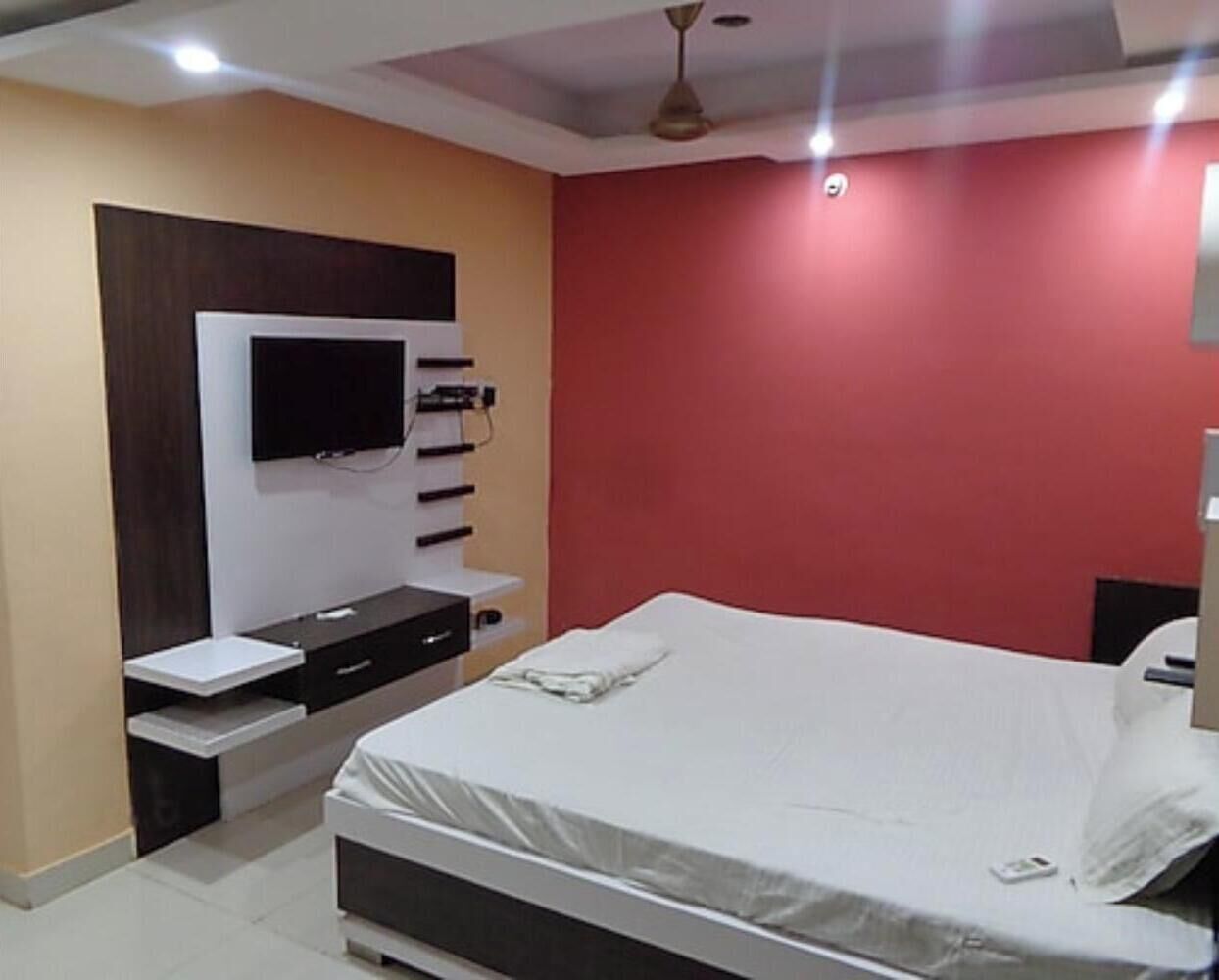 Un dormitorio con cama, televisor montado en la pared y una pared decorativa roja.