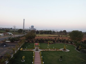 A landscaped garden with pathways, a central walkway, and a tall structure in the background. - Hotel Park Paradise and Restaurant (Gadarwara)
