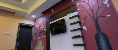 Un interior moderno con una escalera, un televisor de pantalla plana y un mural decorativo con motivos de árboles en la pared.