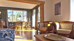 Ein geräumiger Raum mit Holzbalkendecke, einer Essecke mit Holzmöbeln und Bergblick durch große Fenster.