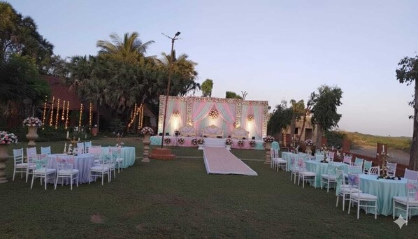 Salón para bodas al aire libre con escenario, mesas y sillas dispuestas en filas.