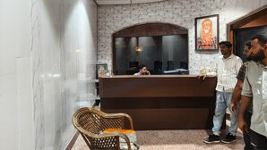 Un espace d’accueil avec un mur en marbre, un comptoir en bois, un fauteuil en osier et un ventilateur de plafond.