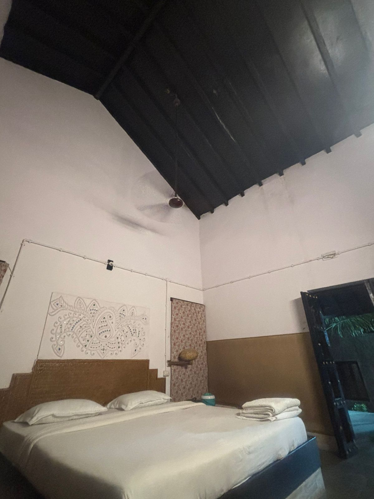A bedroom with a bed, a ceiling fan, a wall with a decorative pattern, and a door.
