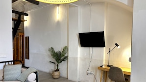 Une chambre moderne équipée d’un lit, d’un bureau, d’une chaise, d’une plante en pot et d’un téléviseur à écran plat fixé au mur.