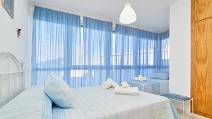Une chambre à coucher comprenant un lit, une table de chevet, une armoire en bois et une fenêtre avec des rideaux légers.