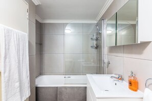 Un baño moderno con cabina de ducha de vidrio, una bañera blanca y un lavabo con dispensador de jabón.