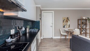 A modern kitchen with a black countertop, white cabinets, and a built-in stove. There is a dining area with a table and chairs, and a bookshelf with decorative items. - The Square 513 by CTHA (Cape Town)