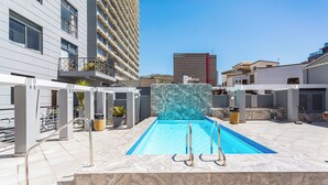 A swimming pool with a marble wall, surrounded by modern buildings and a clear sky. - The Square 513 by CTHA (Cape Town)
