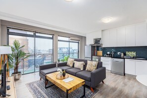 Un apartamento moderno con un sofá gris, una mesa de centro de madera y vistas a la ciudad a través de amplios ventanales.