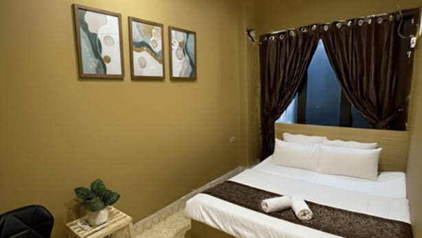 A hotel room with a bed, a small bedside table with a plant, a chair, and three framed artworks on the wall. - NOOK INN OLD QUARTER HANOI (Hanoi)