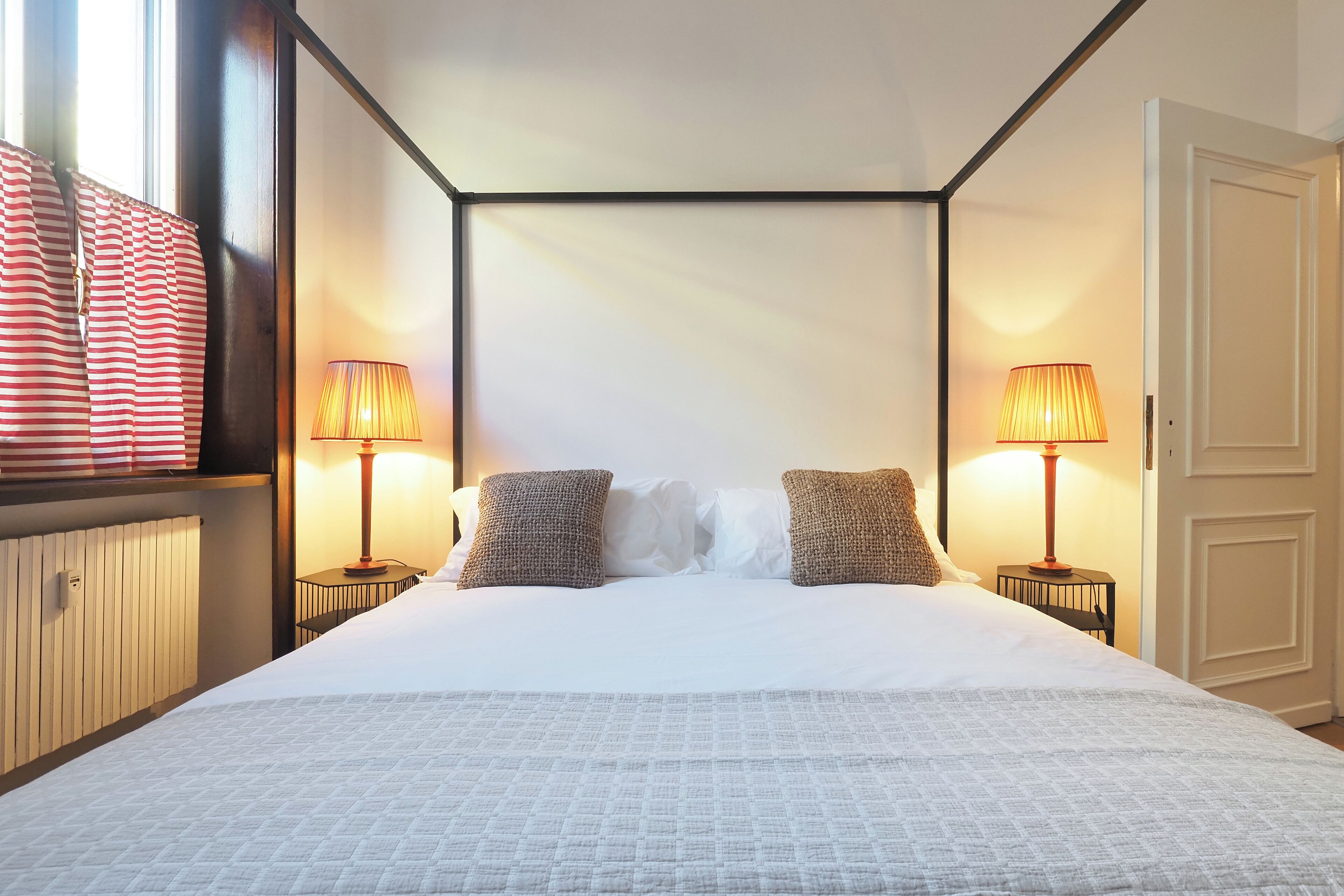 Un lit bien fait, recouvert d’une couette blanche, avec deux coussins à texture et deux lampes de chevet posées sur des tables de chevet assorties.