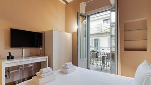 Habitación de hotel con cama, escritorio con televisor, una silla y balcón con mesa y sillas.