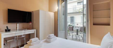 Habitación de hotel con cama, escritorio con televisor, una silla y balcón con mesa y sillas.