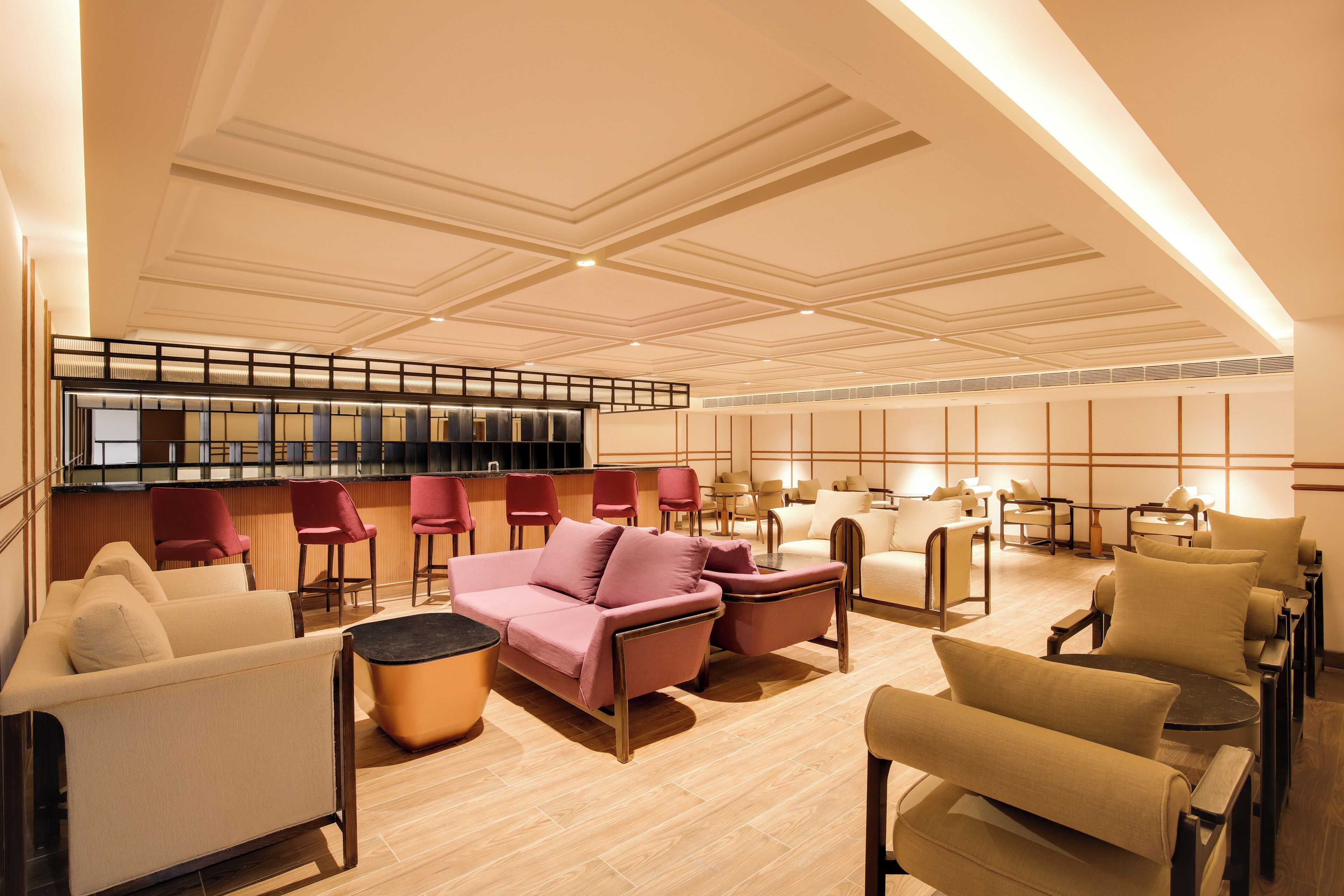 A spacious lobby with a modern design, featuring a mix of seating arrangements including sofas and armchairs, a bar area, and a reception desk.