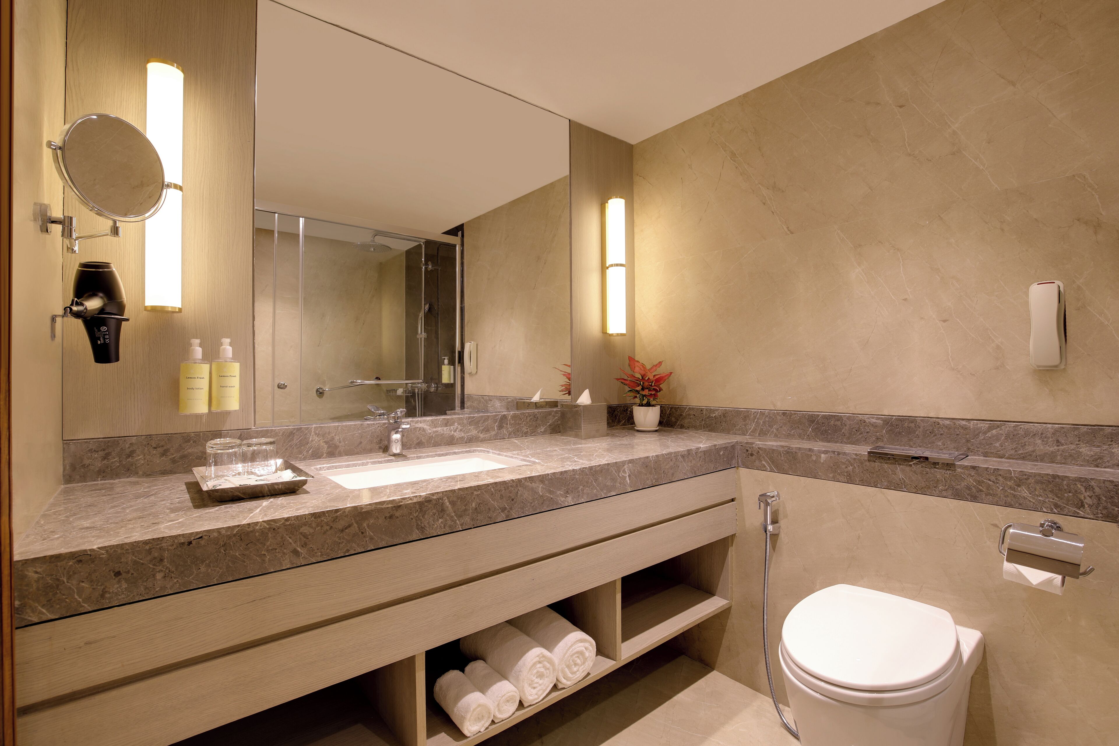 A modern bathroom with a marble countertop, a large mirror, a towel rack, and a toilet.