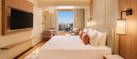 A hotel room with a large bed, a flat-screen TV, a desk, and a view of the city.