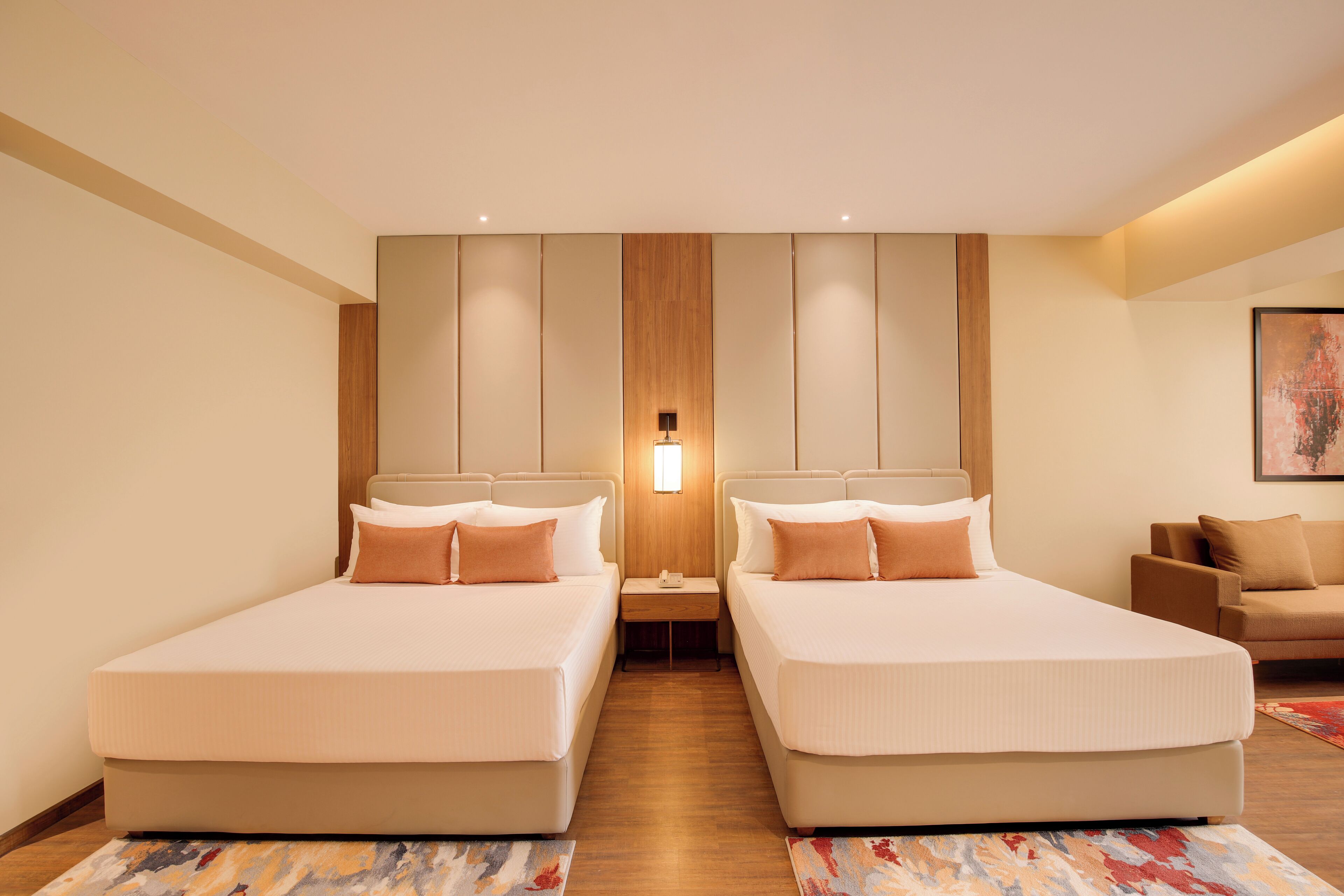 A hotel room with two beds, a nightstand, a sofa, and a painting on the wall.