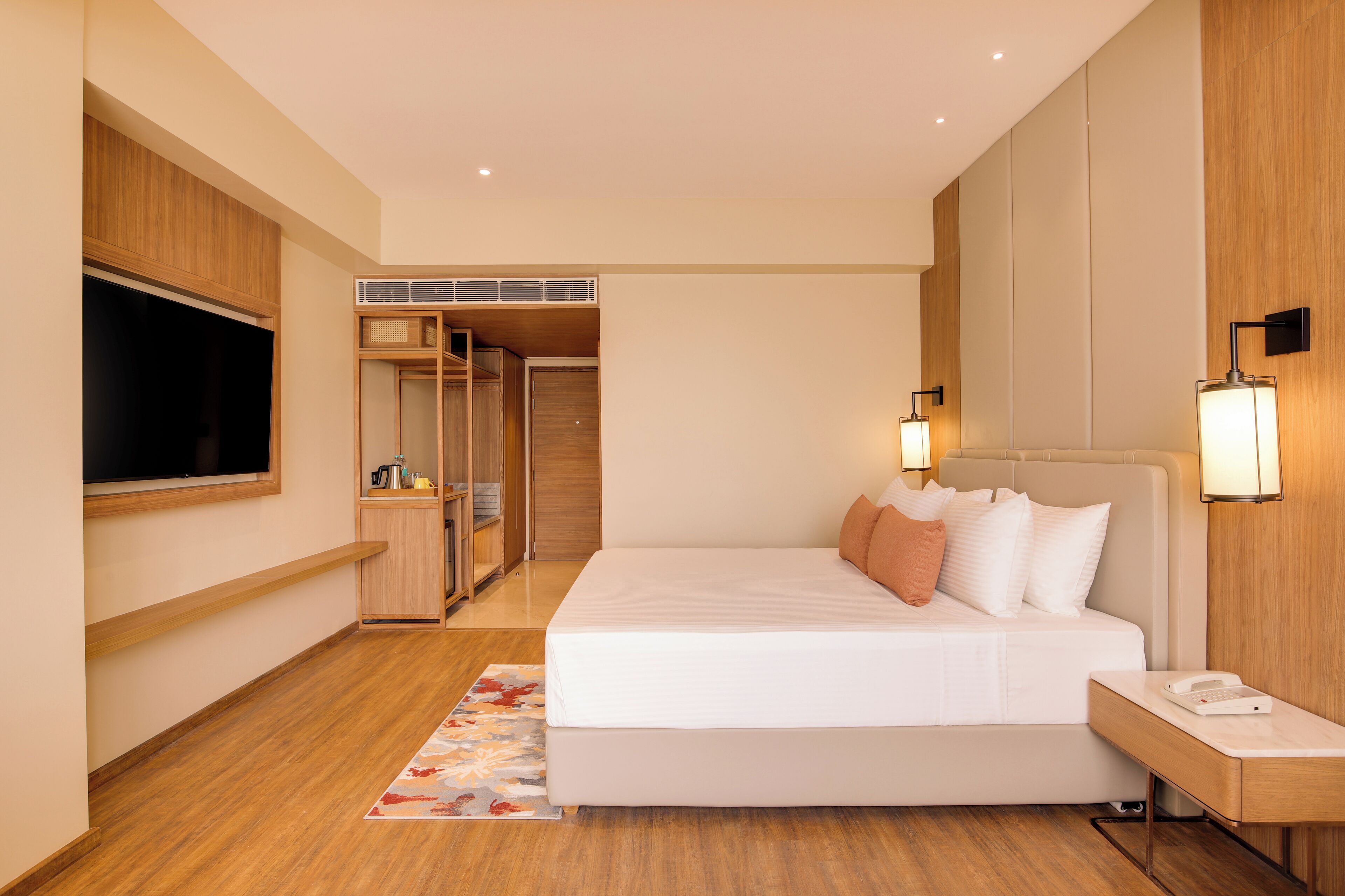 A hotel room with a large bed, bedside lamps, a desk with a phone, a closet, and a window.