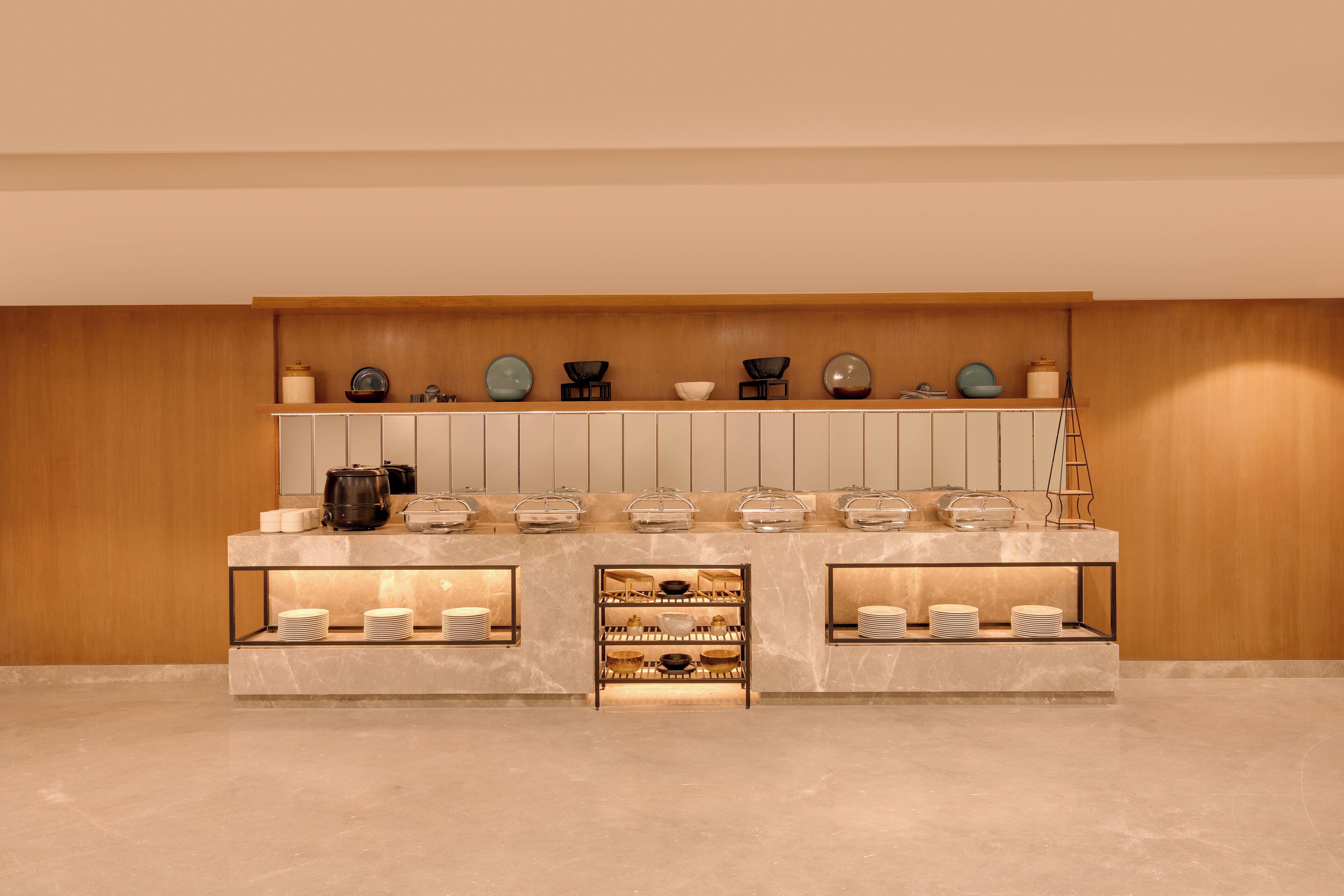 A modern kitchen with marble countertops, a wooden wall, and various kitchenware displayed on shelves.