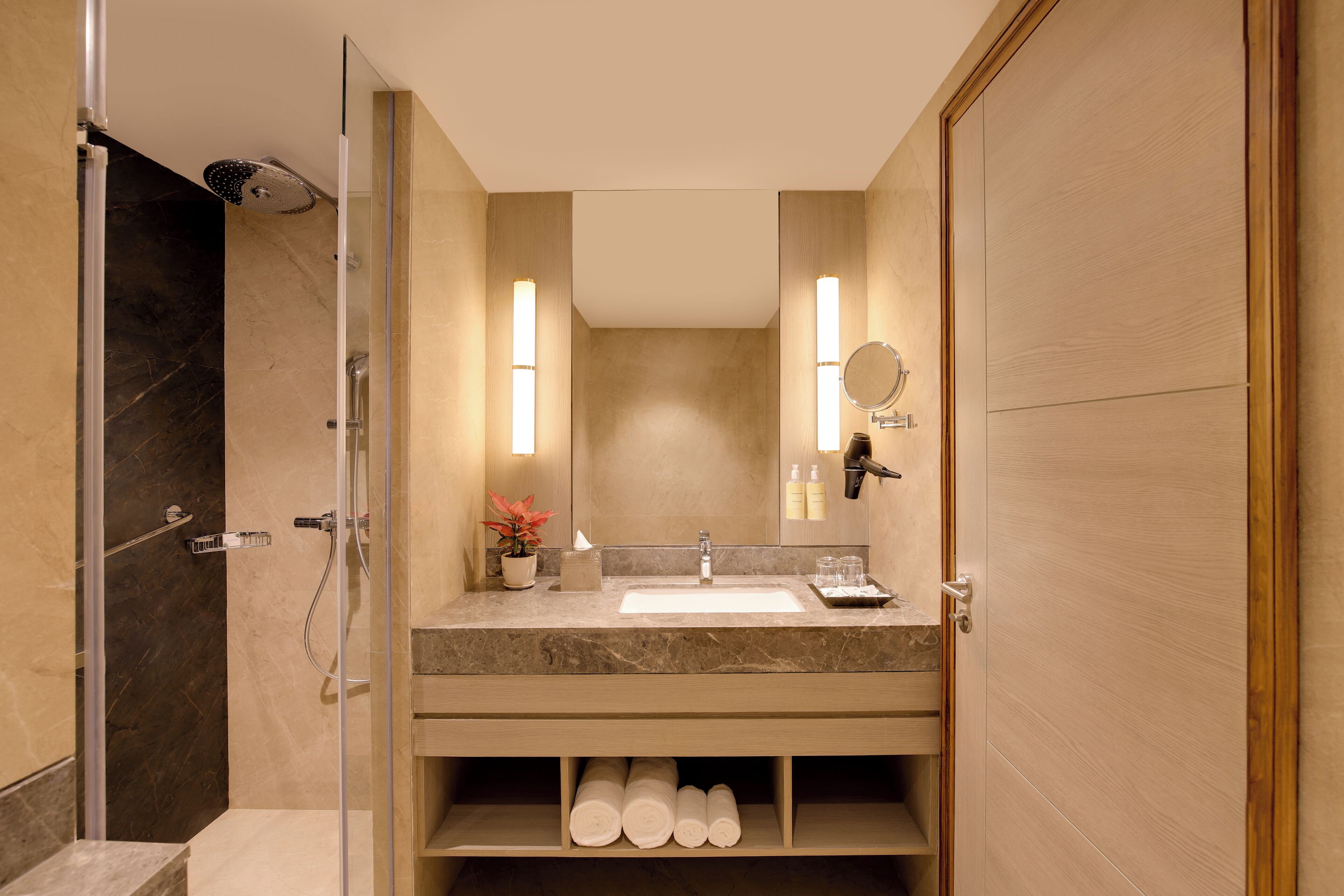 Un baño moderno con cabina de ducha de vidrio, lavabo de mármol y mueble de tocador de madera.
