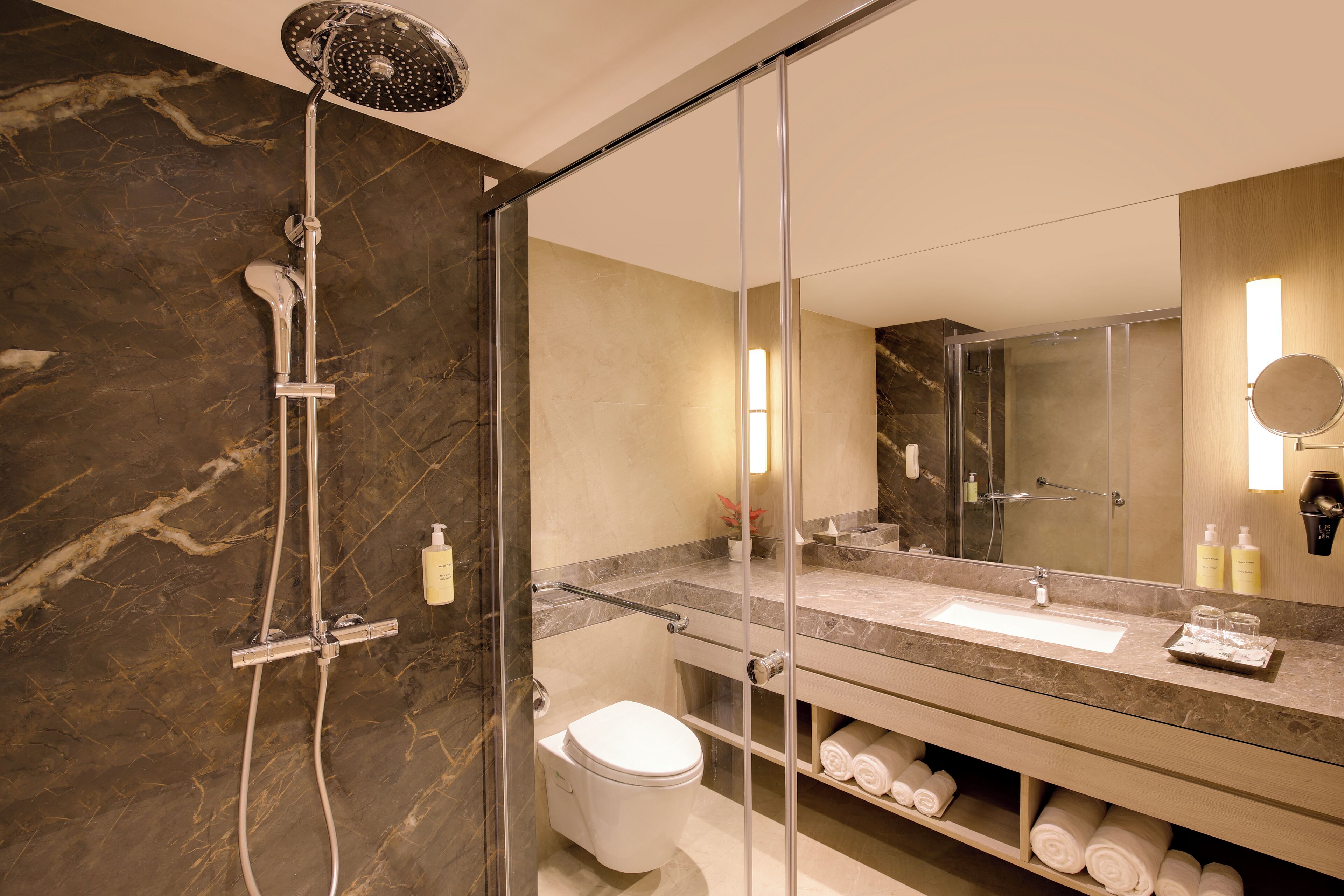 A modern bathroom with a glass-enclosed shower, a marble-tiled wall, a sink with a mirror, and neatly arranged towels.