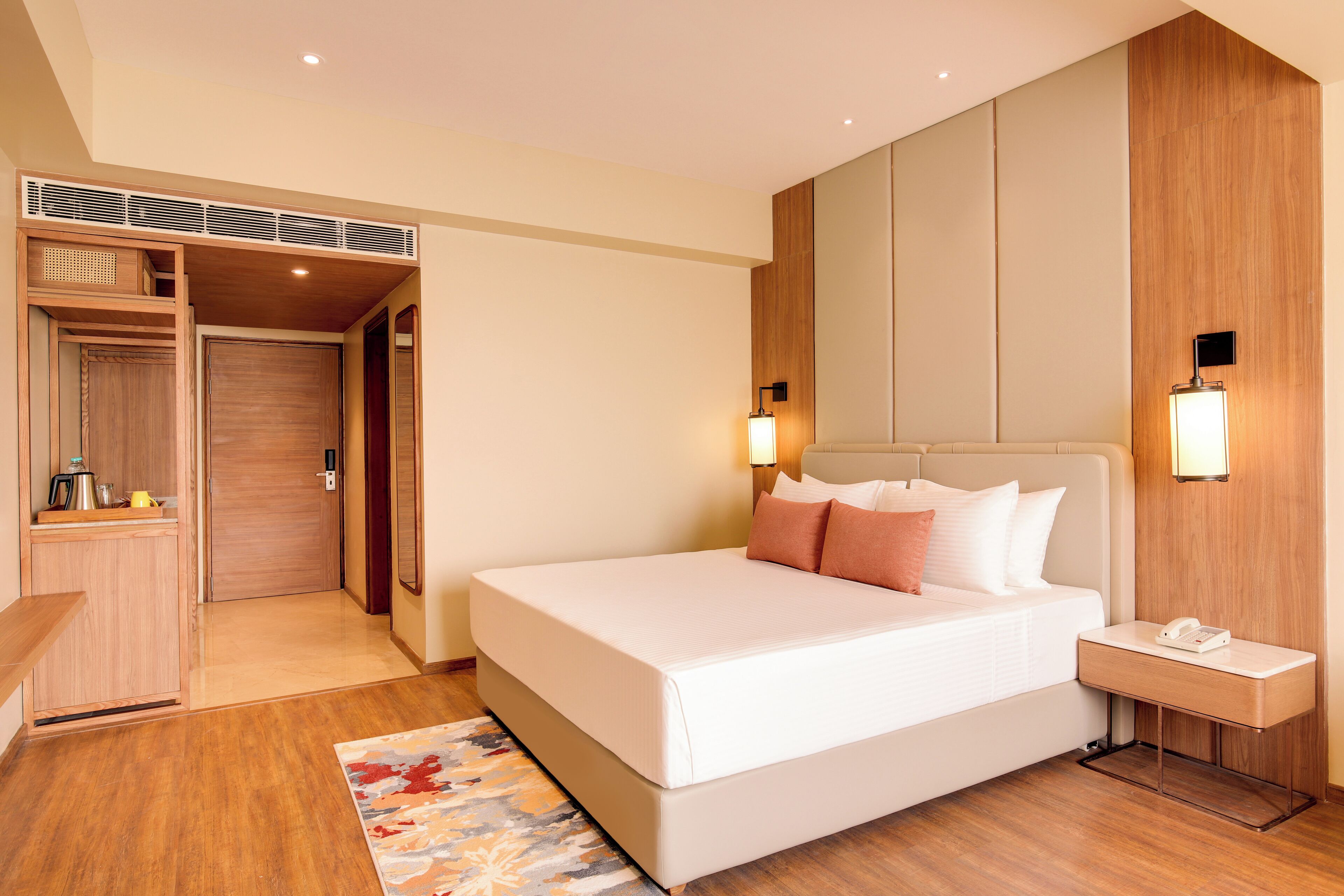 A modern hotel room with a large bed, bedside tables, a wardrobe, and a built-in heater.