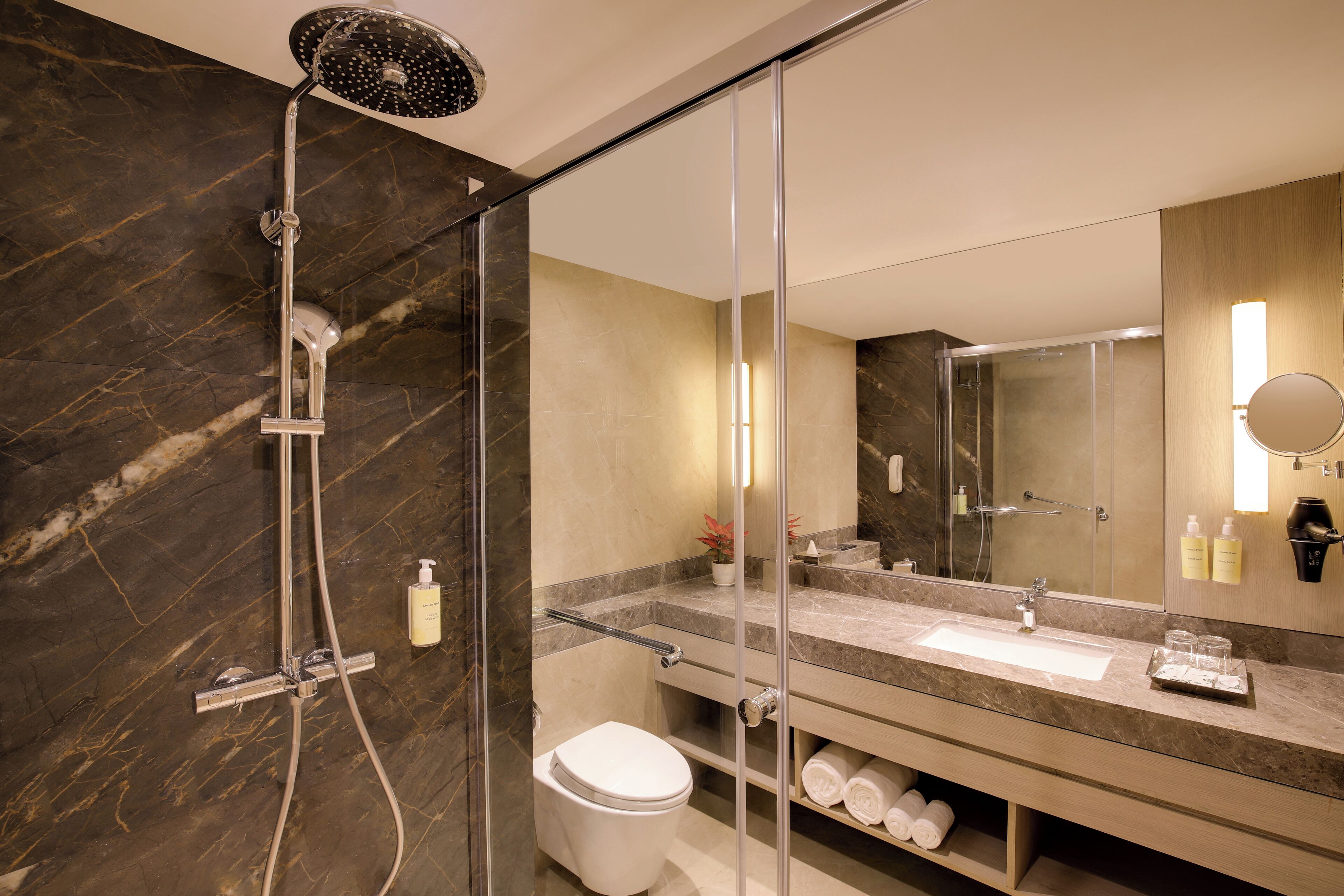 Een moderne badkamer met een glazen douchecabine, een betegelde wand van marmer, een wastafel met spiegel en een toilet.