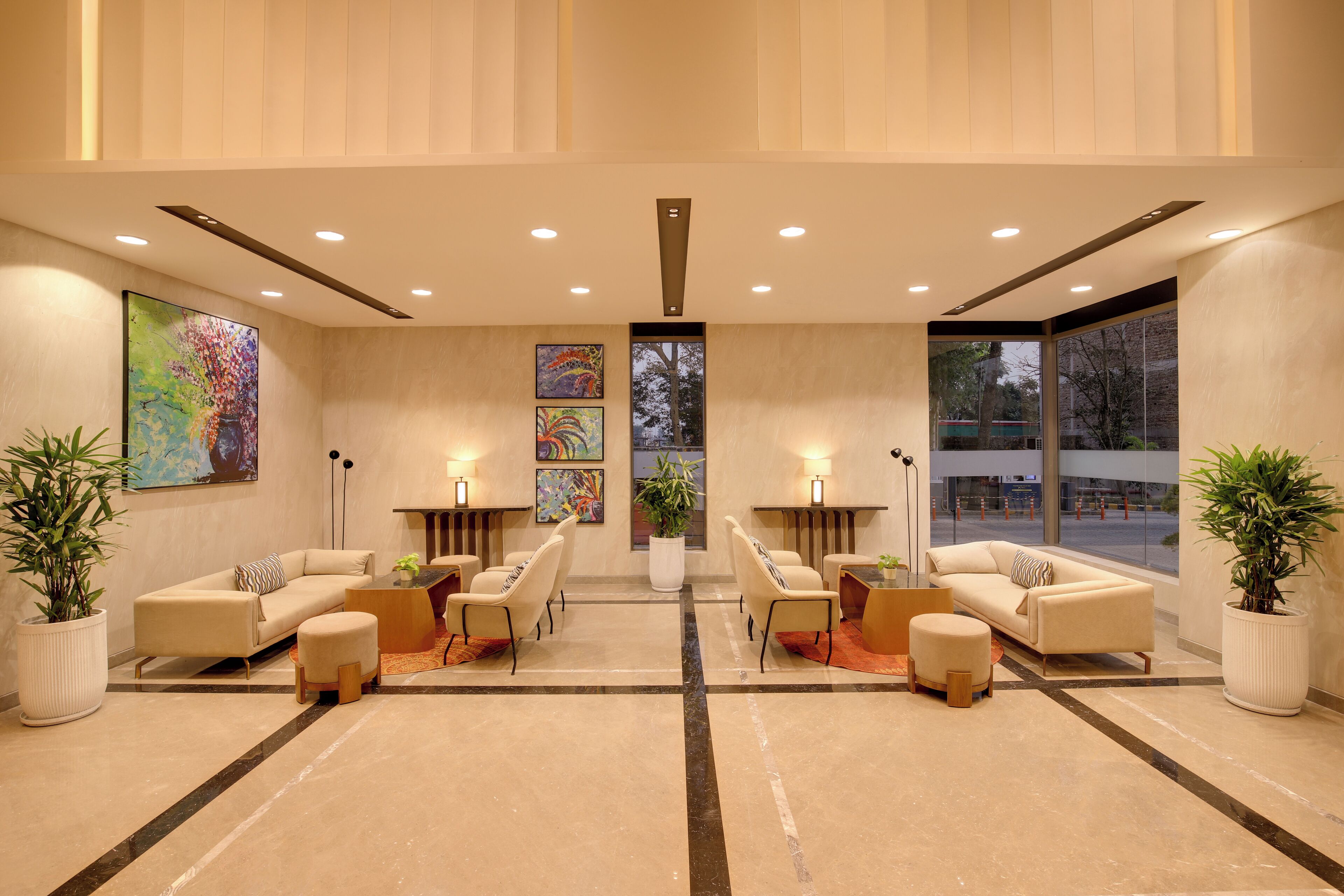 A spacious lobby with two sofas, chairs, and a coffee table, large windows, and artwork on the walls.