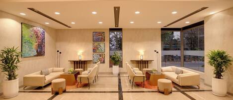 A spacious lobby with two sofas, chairs, and a coffee table, large windows, and artwork on the walls.