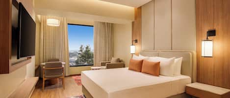 A hotel room with a large bed, a TV, a seating area with a chair and a small table, and a view of the outdoors.