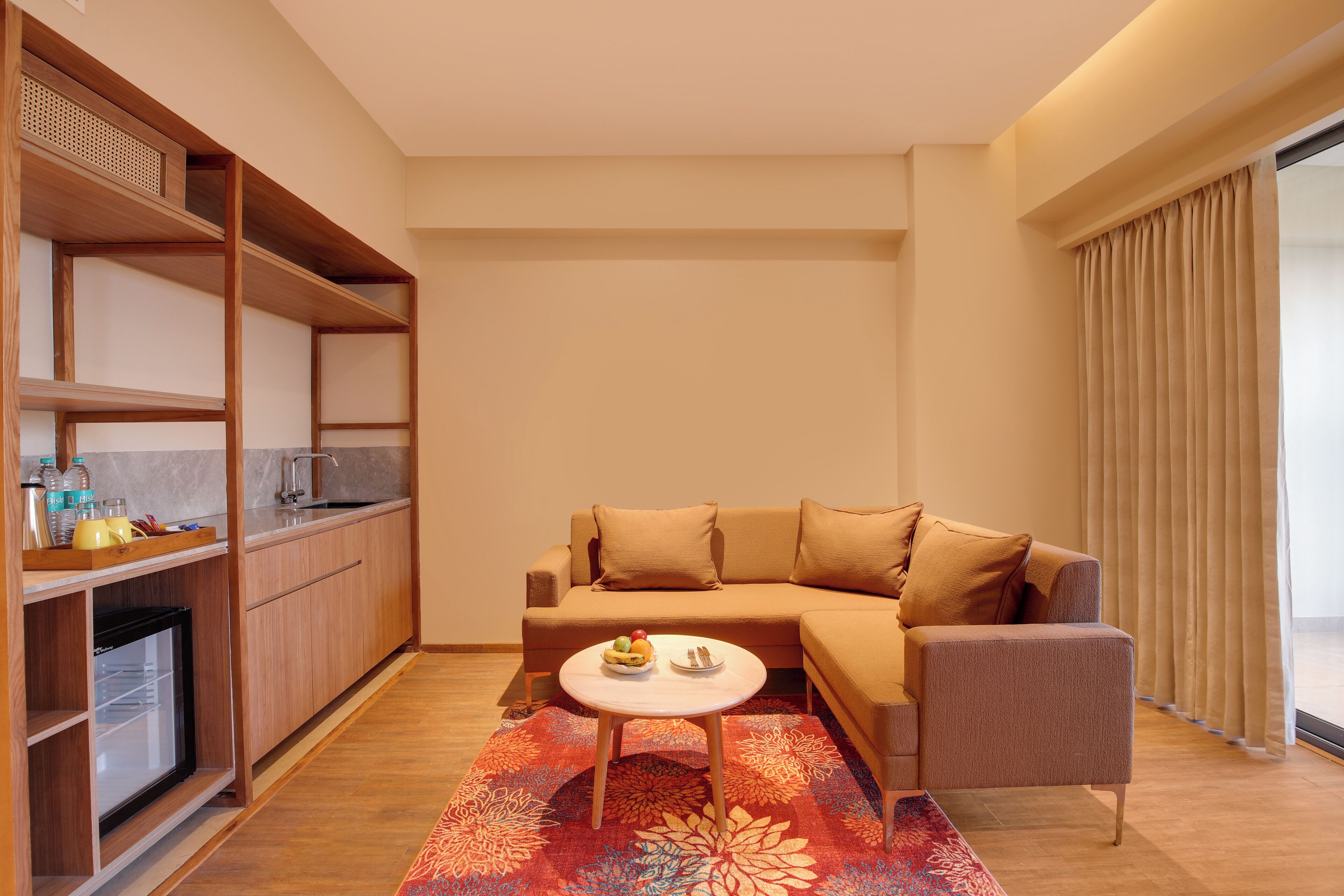 Ein modernes Wohnzimmer mit einer Couch, einem kleinen Tisch und einer Küchenzeile mit Regalen und einem Kühlschrank.