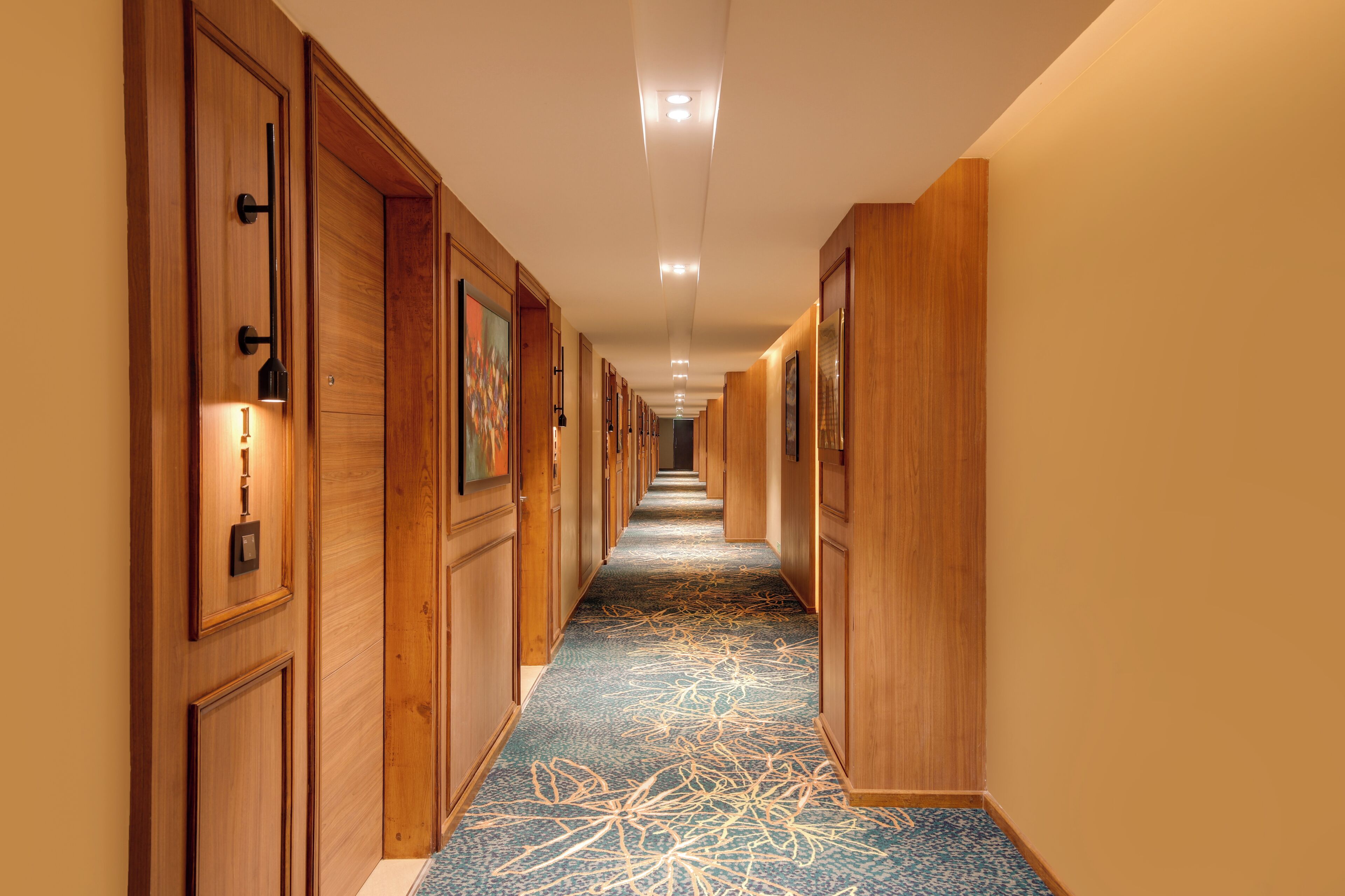 A hotel hallway with wooden paneling, recessed lighting, and a patterned carpet.