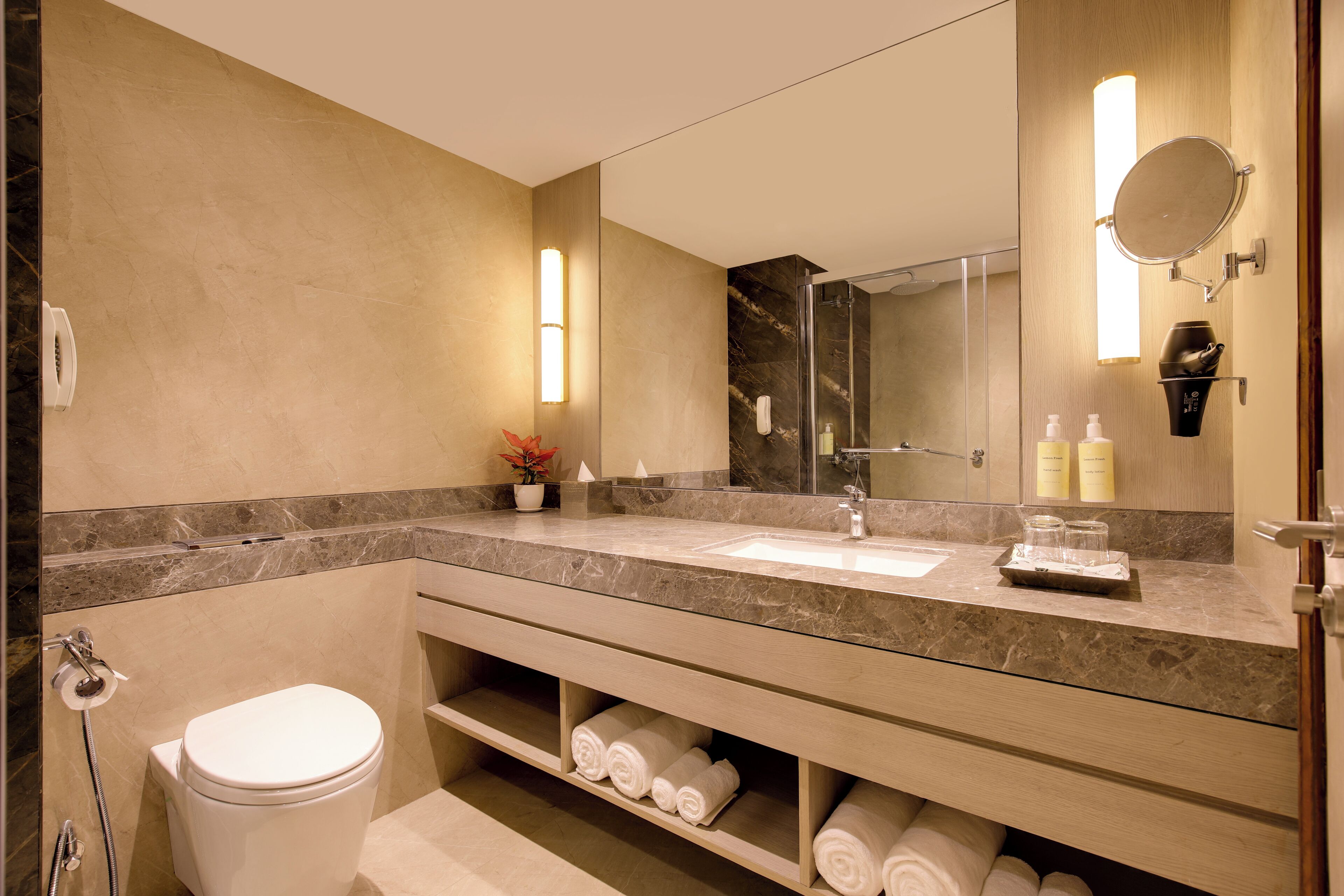 Une salle de bain moderne avec un comptoir en marbre, un grand miroir, des toilettes et une étagère avec des serviettes.
