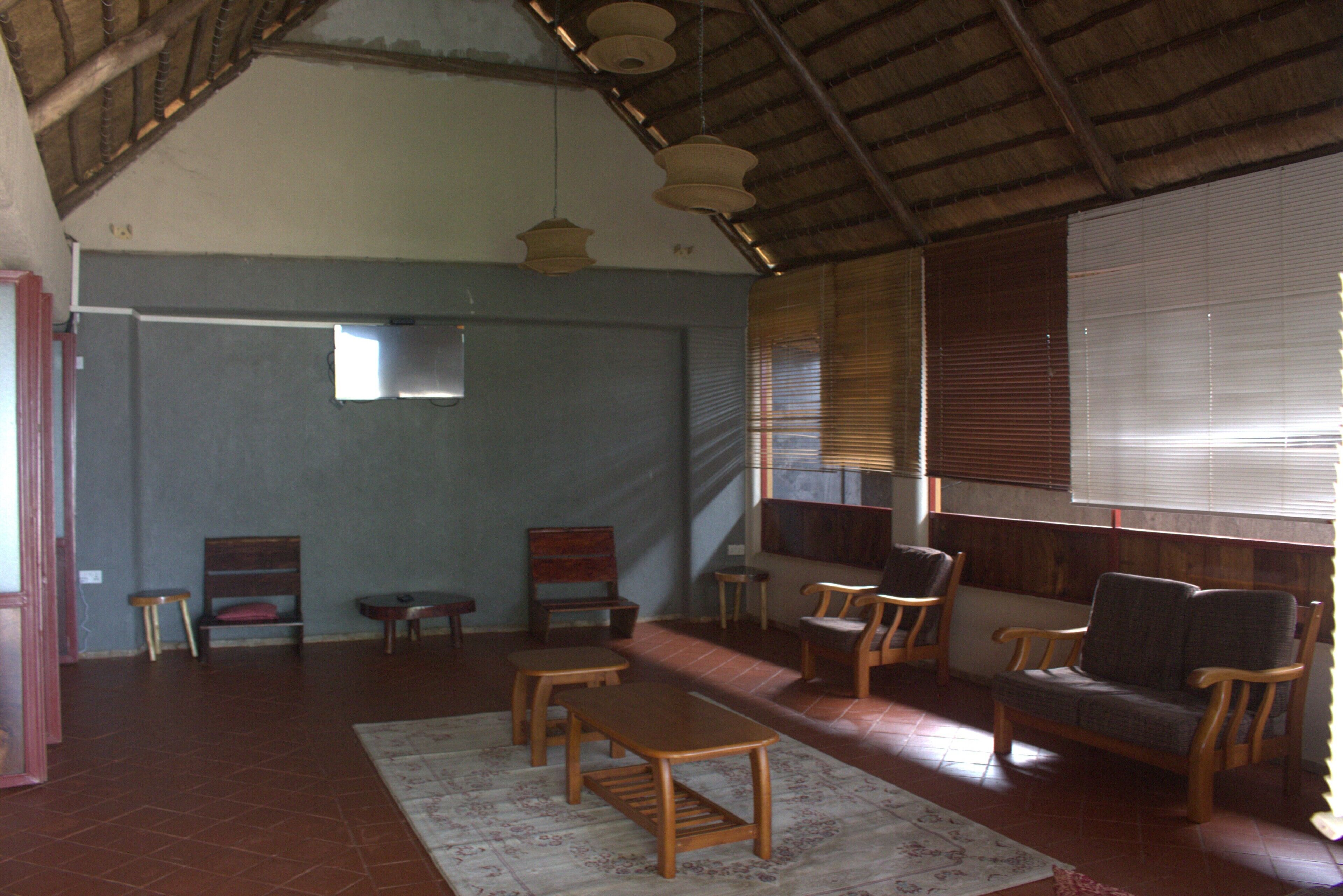 A spacious room with a high ceiling, wooden furniture, and a large window with blinds.
