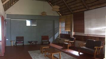 A spacious room with a high ceiling, wooden furniture, and a large window with blinds.