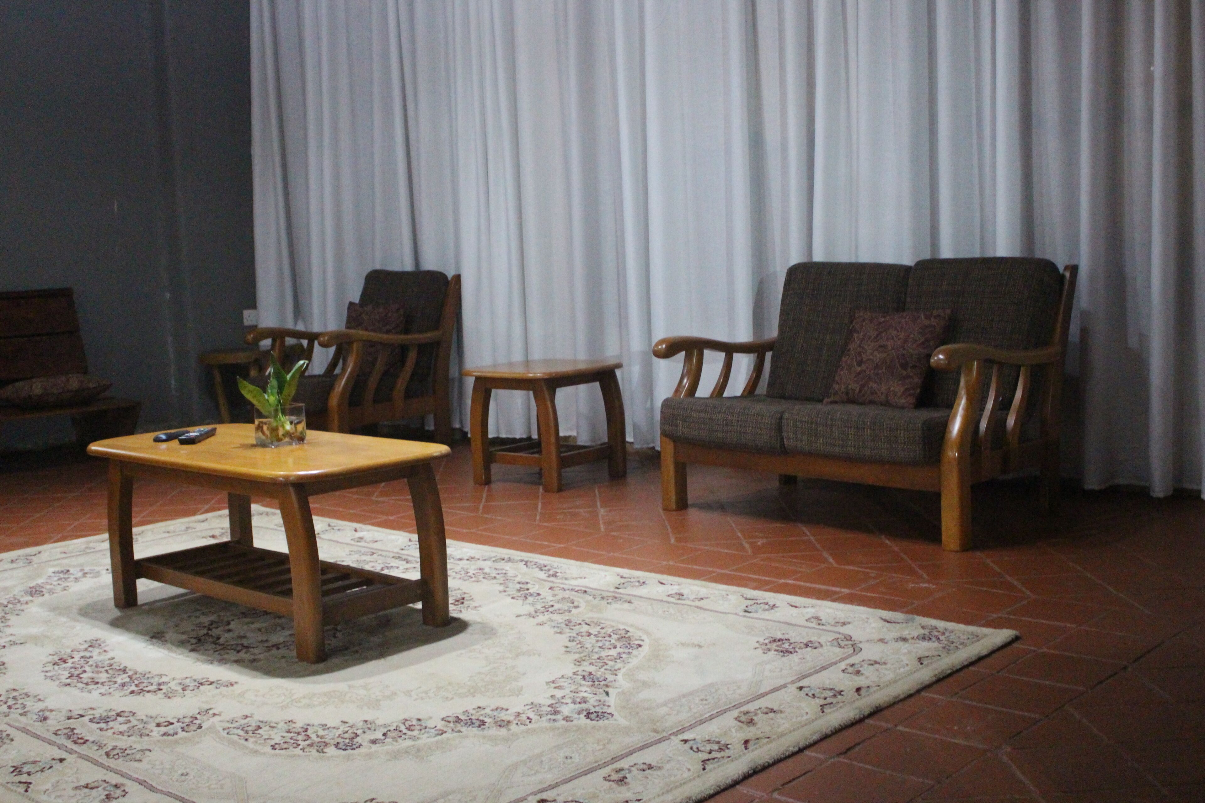 A living room with a wooden coffee table, two armchairs, a small side table, and a patterned rug on a tiled floor.