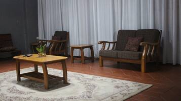 A living room with a wooden coffee table, two armchairs, a small side table, and a patterned rug on a tiled floor.