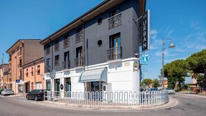 A multi-story building with a storefront, a parking sign, and a pedestrian crossing. - Urban Hotel (Cesena)