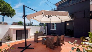 An outdoor patio with wicker furniture, a large umbrella, and a tiled floor. - Urban Hotel (Cesena)