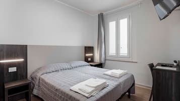 Quarto de hotel moderno com uma cama grande, mesas de cabeceira, escrivaninha e televisão fixada na parede.