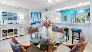 A modern kitchen with a round glass table, wicker chairs, and a vase of flowers.