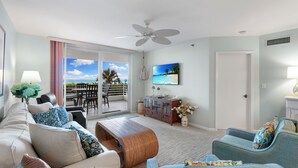 A spacious living room with a large window, a ceiling fan, and a television.